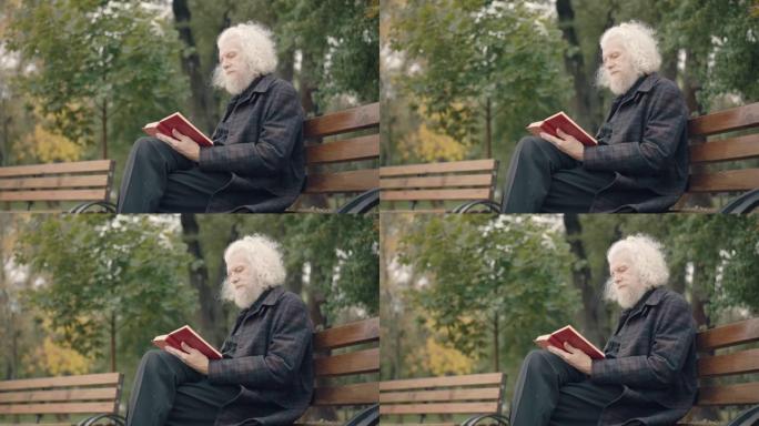 秋天公园读书的集中老人坐在长凳上的侧视图。吸收了白人男性退休人员，退休后在户外享受业余爱好。生活方式