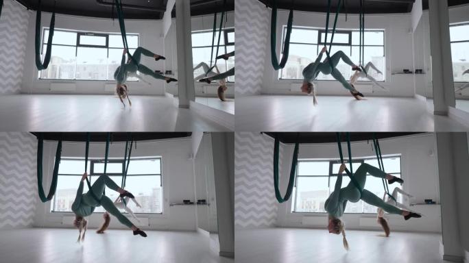 两名年轻的瑜伽士妇女在健身俱乐部的绿色吊床上进行空中瑜伽练习。美丽的女性在课堂上锻炼，表演航空瑜伽。