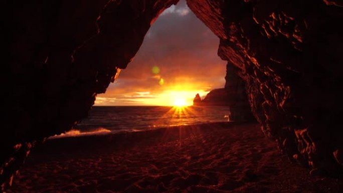 从日落，大海和海滩上的石洞可以看到，温暖的夕阳照亮了洞穴的火山岩。冰岛的火山玄武岩。美丽的世界，自然