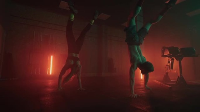 一男一女一起在健身房做倒立慢动作。一个坚强的男人和一个女人在倒立的情况下穿着彩色油灯走过健身房的地板