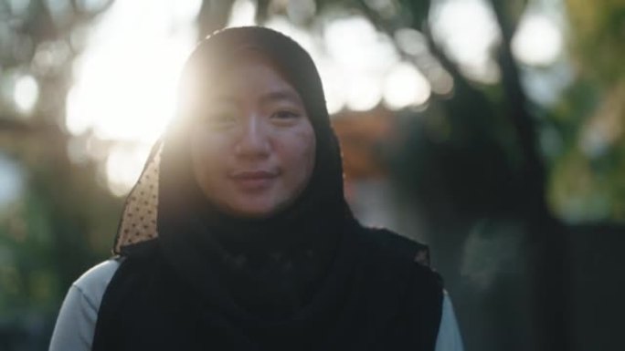 亚洲马来妇女戴着头巾，白癜风皮肤状况，早上看着相机在后院花园微笑