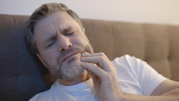 40多岁的悲伤男性躺在床上，患有急性牙痛，牙齿健康