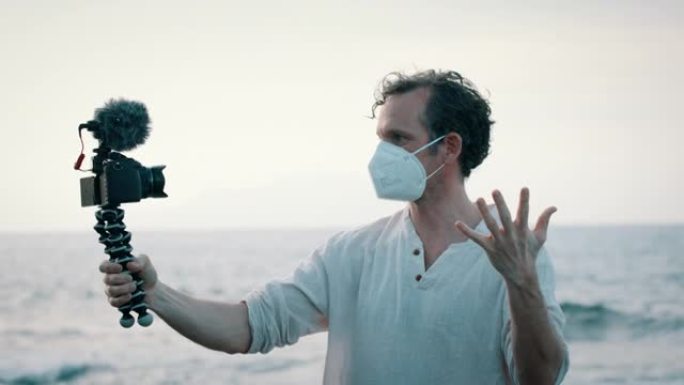 戴着口罩的男子在海洋附近与手持摄像机交谈