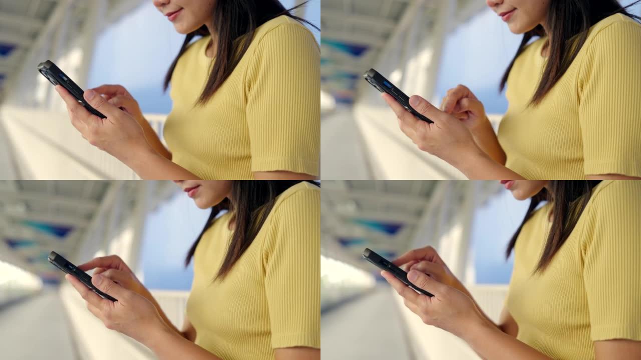 亚洲女子在玩手机的路上连接车站在线购物和社交媒体。