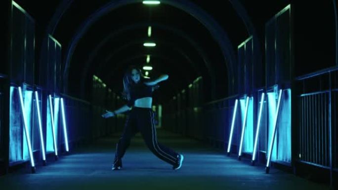 性感苗条的女人在黑暗的隧道里用神秘的蓝光跳舞
