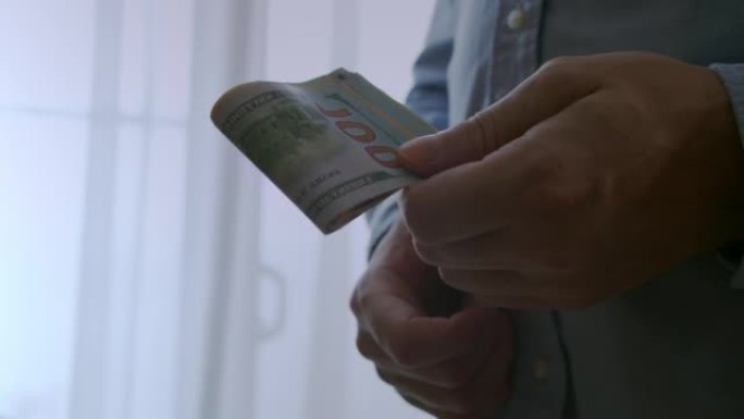 一名男子从他的衬衫口袋里拿出100美元钞票，数了数钱，然后把它对折，放进他的衬衫口袋里。资金不足，手