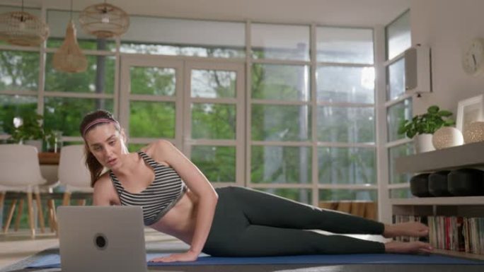 女运动员在瑜伽垫上做腿部锻炼和阅读。放松的家庭锻炼