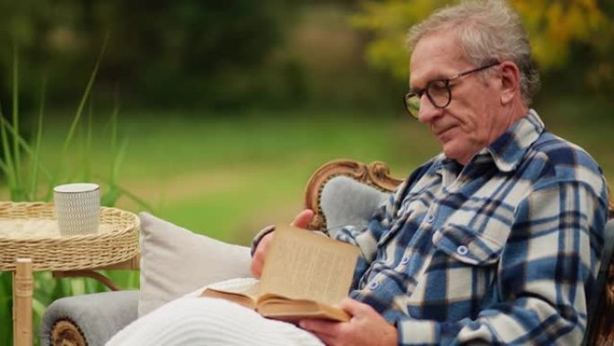 生病的老年男性患者在外面的椅子上看书