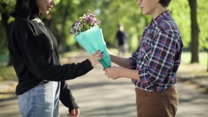 侧视图无法辨认惊讶的十几岁的女孩从爱心男孩那里收到一束鲜花。害羞的高加索青少年夫妇在阳光明媚的夏日公