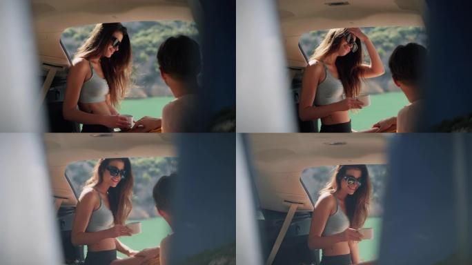 可爱的年轻夫妇坐在美丽的绿松石湖边的汽车后备箱里喝茶