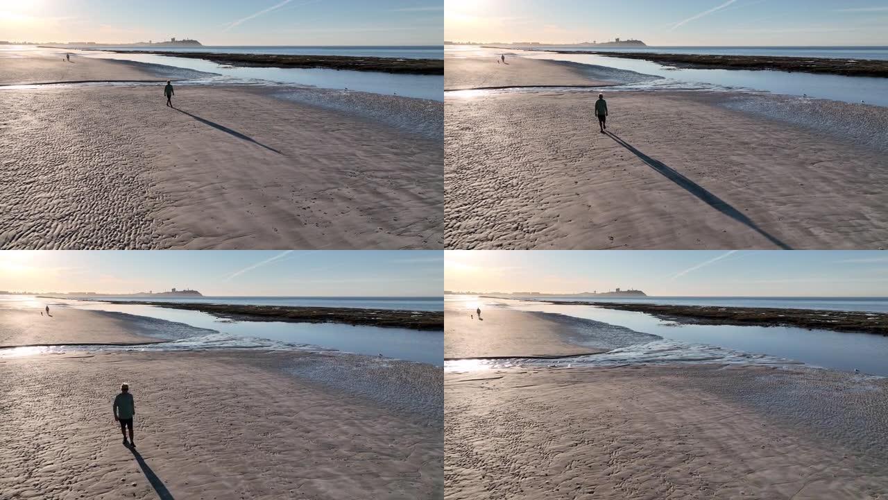 男子在空旷的海滩上漫步的鸟瞰图