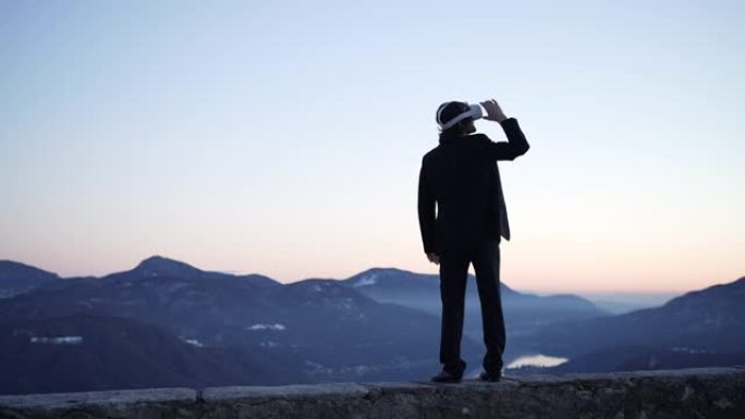 男子在山间户外戴着VR虚拟现实护目镜，日落时可以看到下面的湖