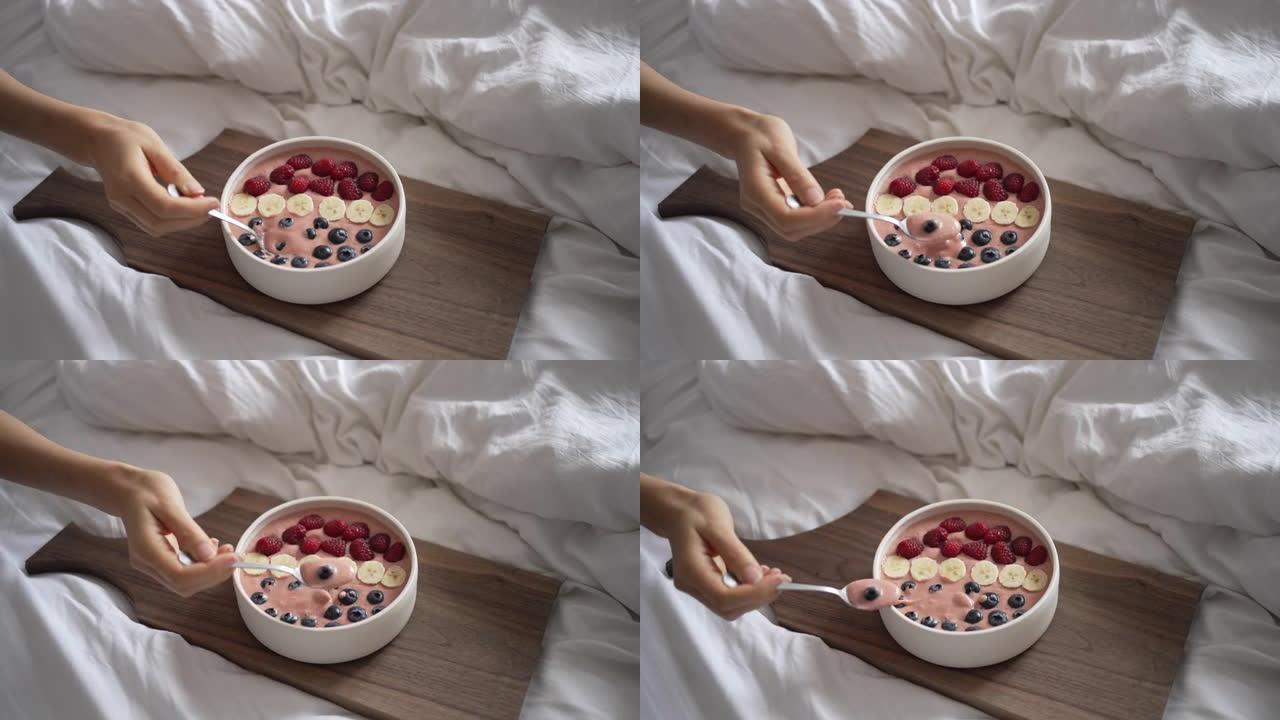 手持勺子拿起浆果，在床上吃早餐的细节