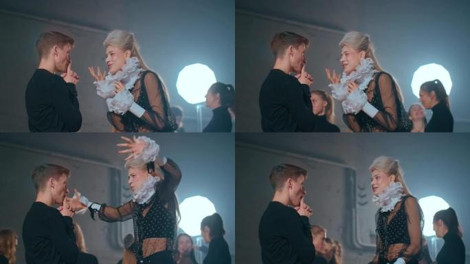 侧视专业熟练的女演员和演员排练角色，模糊的同事在背光背景训练。积极自信的白人男女谈话准备表演。