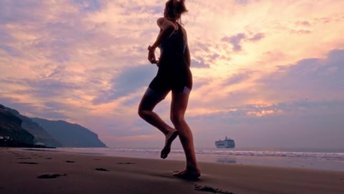 女人赤脚在海滩上慢动作跑步。日落sihouette
