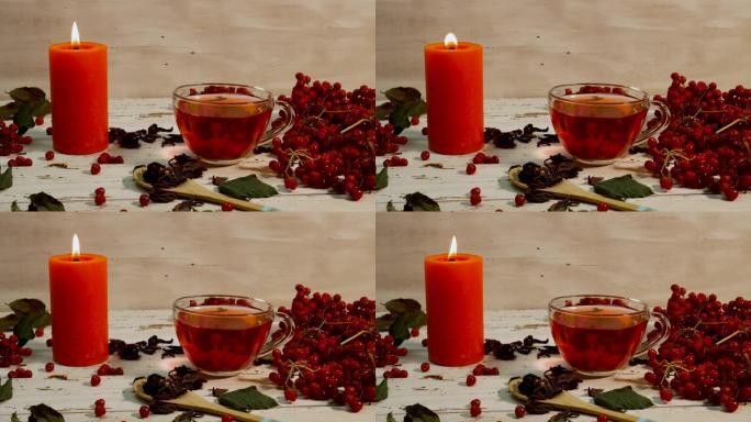 在白色的木桌上放红茶和燃烧的蜡烛的杯子。木制乡村木板上的红色荚果浆果中的天然茶。自然疗法愈合输液。抗