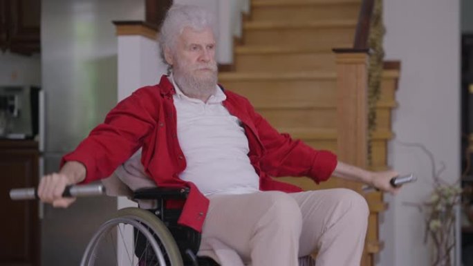 自信的老年残疾英俊男子坐在轮椅上在室内慢动作举起哑铃。动机高加索残疾人退休人员在家训练的肖像。运动和