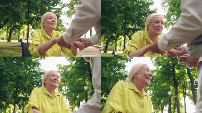 快乐的老年妇女试图在丈夫的帮助下从轮椅上站起来