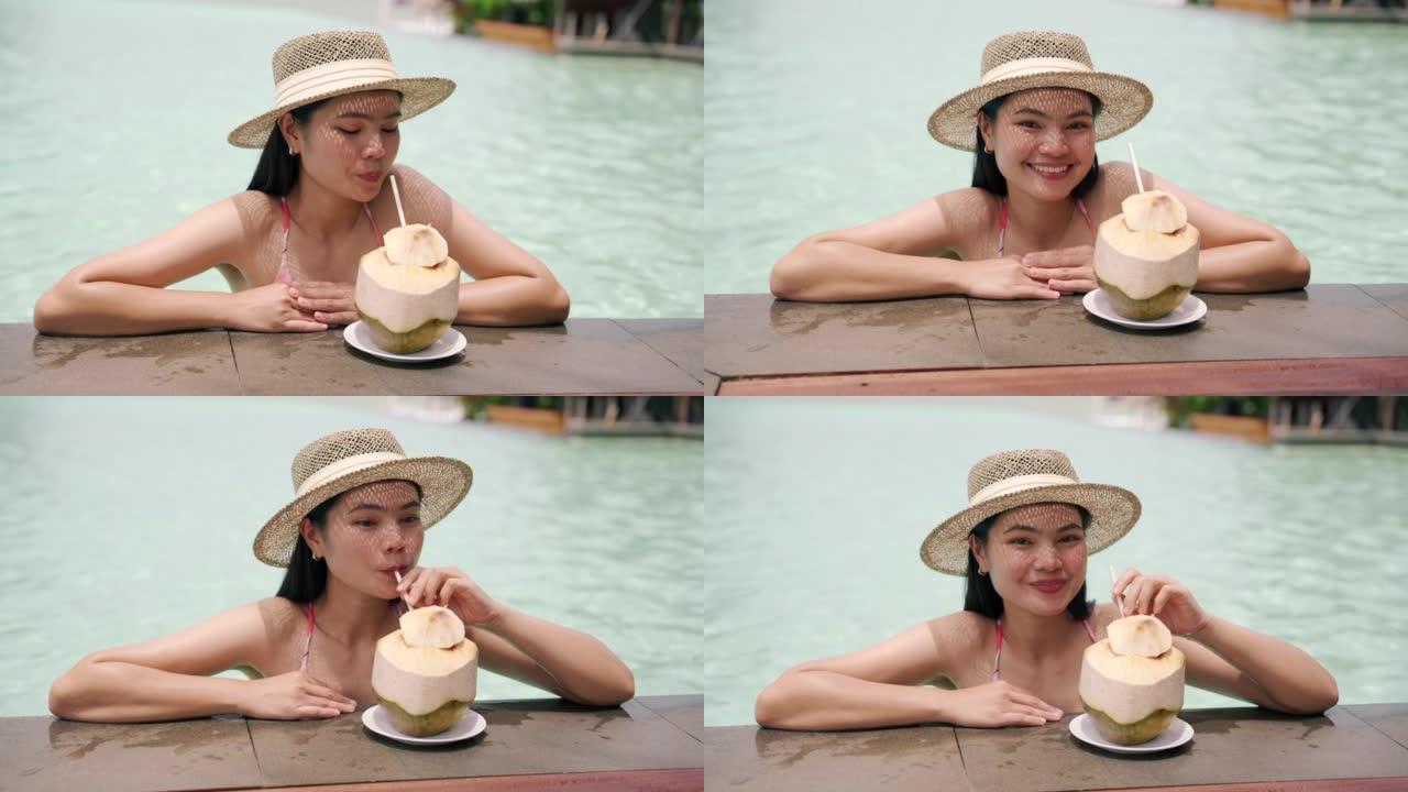 穿着比基尼泳装和太阳帽的亚洲女孩在游泳池边喝椰子水放松。