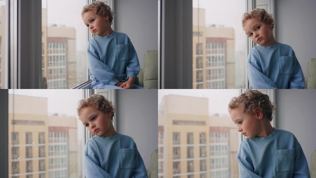 沉思的四岁男孩正在舒适的现代公寓里看着房间窗户上的积雪
