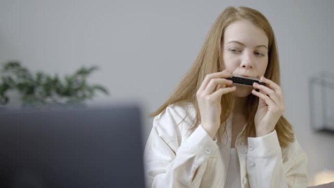 快乐的年轻女性学习如何演奏口琴，在笔记本电脑上观看教程