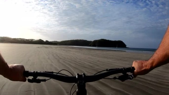男子在日出时沿着空旷的海滩骑自行车