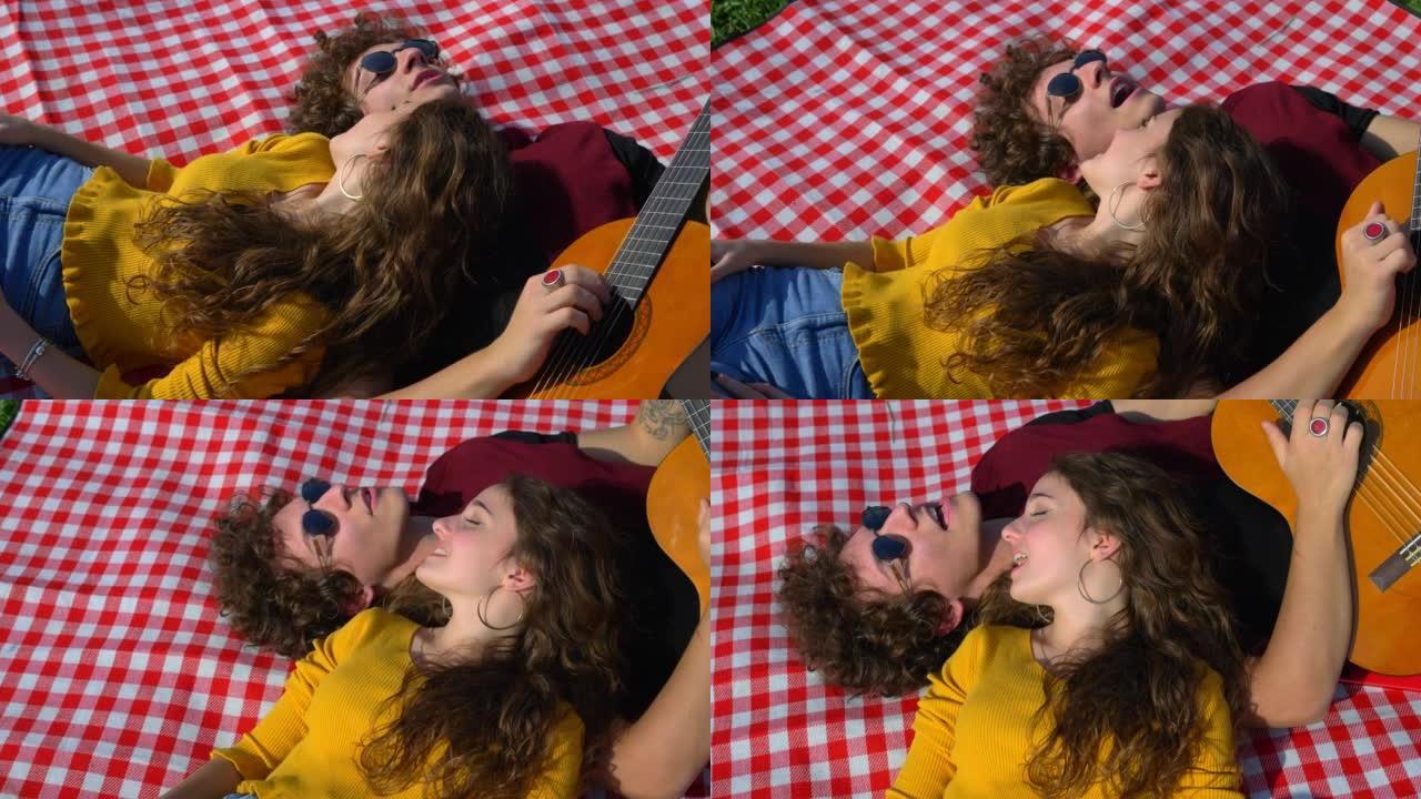 公园的二重唱-躺在草坪上的年轻无忧无虑的夫妇唱歌和弹吉他