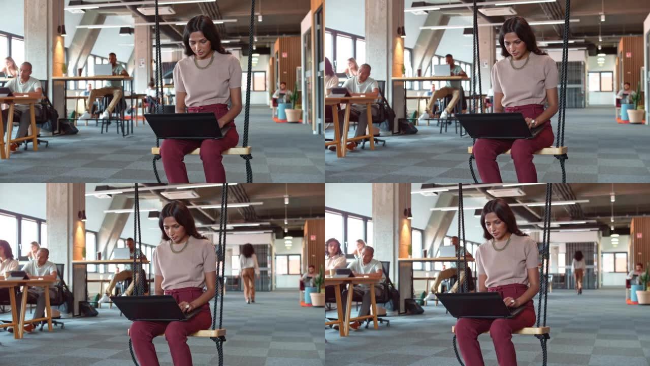 DS年轻女子坐在办公办公室的秋千上，在笔记本电脑上工作