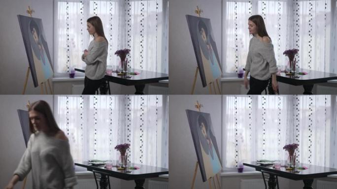侧视肖像苗条的年轻女子看着画架上的照片摇摇头叹息离开。不满意的高加索艺术家对绘画结果不满意。失去灵感