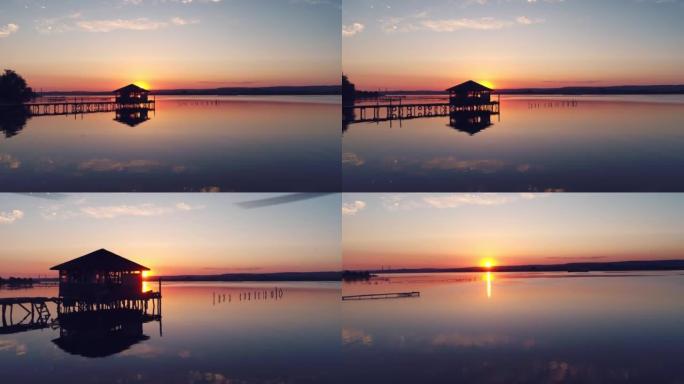 在美丽的日落时分，缓慢而平稳地在湖上钓鱼码头和海水中的旧平房上移动