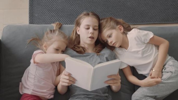 家庭阅读时间。三个小姐妹在沙发上看书，拥抱