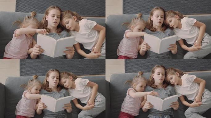 家庭阅读时间。三个小姐妹在沙发上看书，拥抱