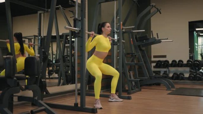在健身房或健身俱乐部使用机上健身史密斯机锻炼西班牙裔年轻女性锻炼身体肌肉。女孩用杠铃在肩膀上举重，同