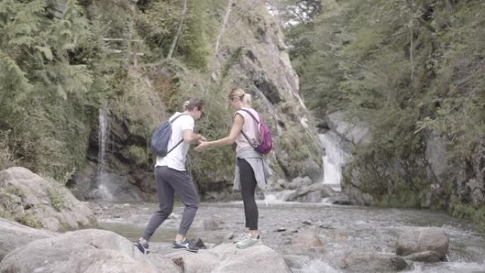 年轻夫妇站在河边的岩石上，面对着