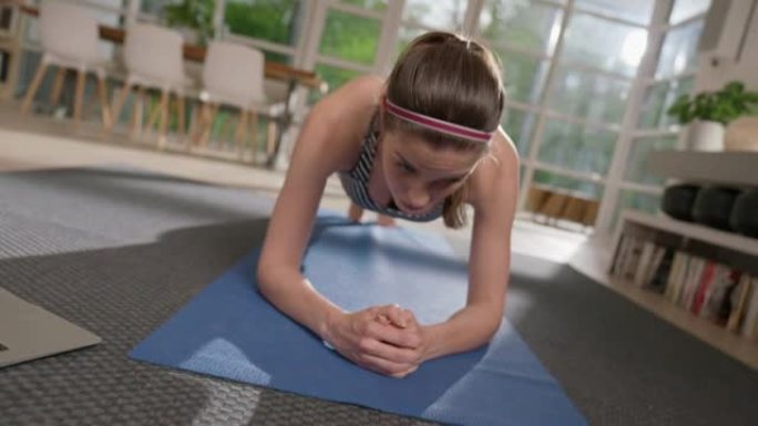 女运动员用笔记本电脑在瑜伽垫上做木板。家庭锻炼。纺纱效果
