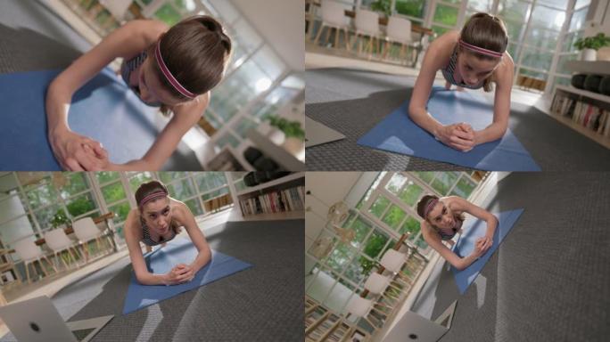 女运动员用笔记本电脑在瑜伽垫上做木板。家庭锻炼。纺纱效果