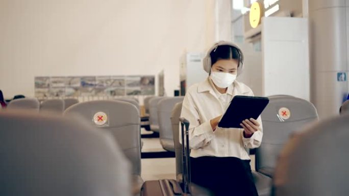亚洲妇女在机场出发区使用数字平板电脑戴口罩。