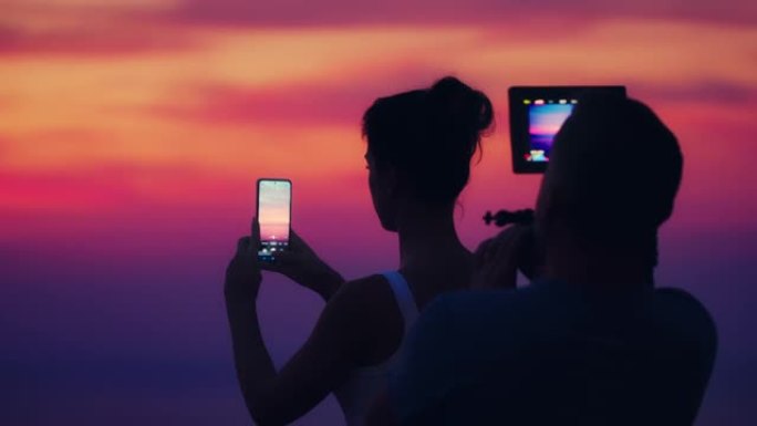 在露台上开会。背景中的女人拍摄史诗般的日落照片。摄影师设置相机