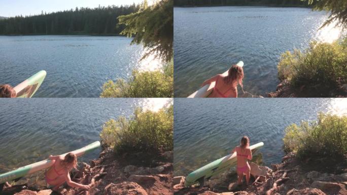 年轻女子在站立桨板 (SUP) 上进入湖中