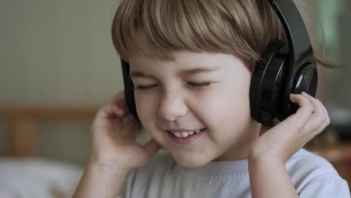 戴着耳机听音乐的可爱的小男孩的肖像。孩子戴着耳机闭着眼睛放松时的慢动作。孩子在家听音乐。快乐无忧无虑