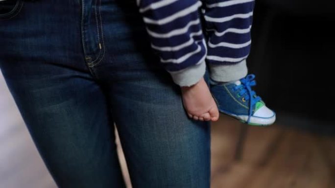 女婴的赤脚腿和运动鞋的脚特写。面目全非的高加索母亲抱着小女儿，双手垂下，孩子的腿。