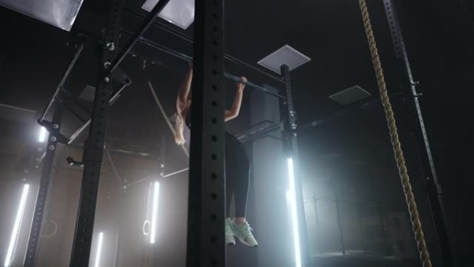 强壮的女运动员在健身房做引体向上，晚上在黑暗的健身馆独自训练