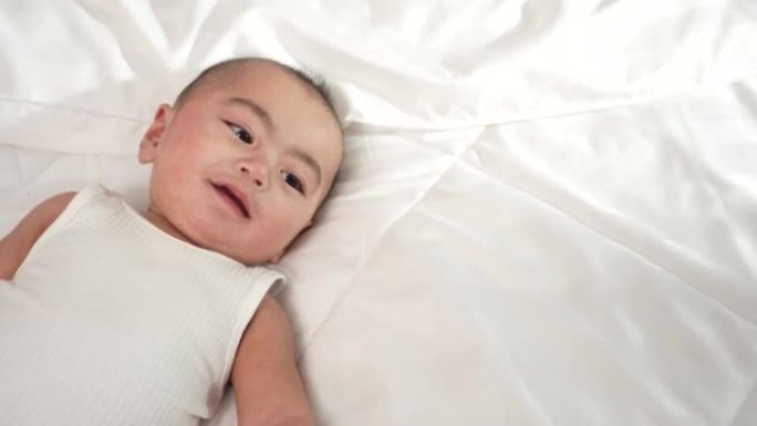 初生婴儿或可爱的小家伙躺在家里的白色床上微笑。婴儿儿童肖像快乐概念，早上健康育儿。