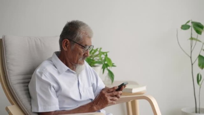 老年男子坐在扶手椅上使用电话休息