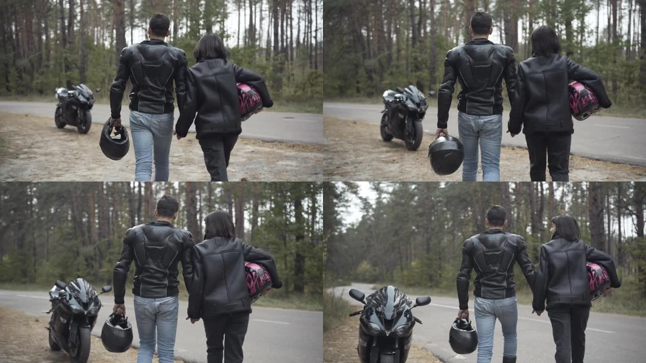 自信的几个摩托车手牵着手沿着路边走过黑色时尚摩托车的后视图。镜头跟随跨种族的爱男人和女人在户外漫步。