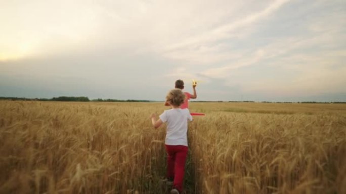 无忧无虑的快乐孩子在黑麦或小麦的金色田野中奔跑，玩玩具飞机，后视图