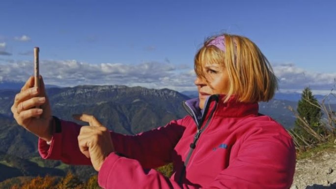 SLO MO高级女徒步旅行者坐在山顶上，用智能手机检查附近的山峰