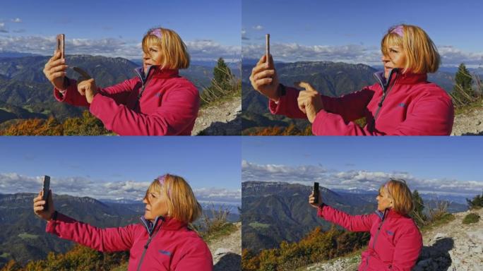 SLO MO高级女徒步旅行者坐在山顶上，用智能手机检查附近的山峰