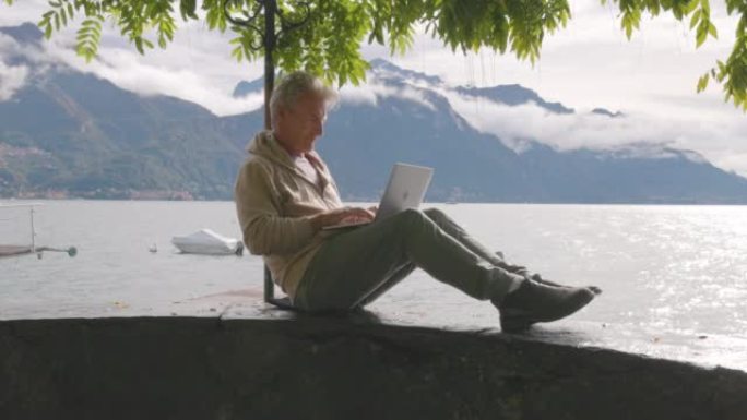 成熟的男人在湖畔栖息使用笔记本电脑