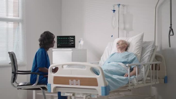 一名黑人女性心脏病专家医生正在与一名躺在病床上的老人患者交谈，讨论康复后的康复。传染病神经科医生讨论